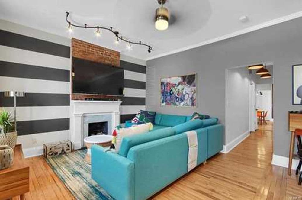 Modern living room with striped walls, teal sectional sofa, and stylish decor.