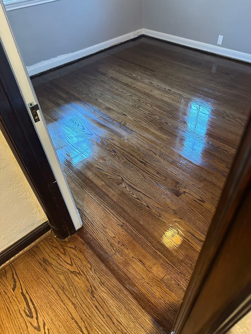Shiny hardwood floor in a well-lit room with a doorway view.
