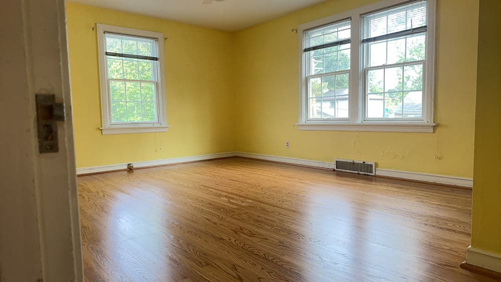 Empty room with yellow walls and hardwood flooring, featuring large windows for natural light.
